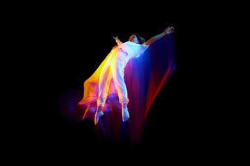 Levitation. One flying, jumping dancer or gymnast performing tricks in the air over black background with mixed neon glowing rays