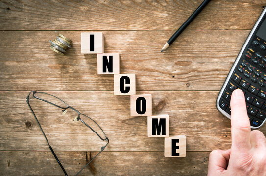 Blocks with black letters saying Income on wooden background with hand on calculator