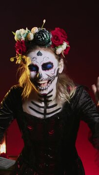 Vertical video: Horror goddess of death yelling in costume with skull body art, wearing flowers crown and screaming like holy santa muerte to celebrate dios de los muertos. Woman on tranditional