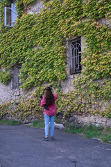 Fototapeta na wymiar A building covered with ivy, woman taking photo of an old building, woman in pink shirt, tourist concept idea photo. 