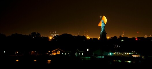 Statue of Liberty before an orange scenic half-moon at night