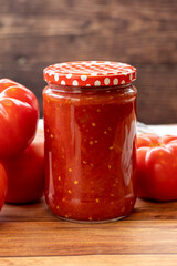 Canned tomato sauce in glass jar on wood background