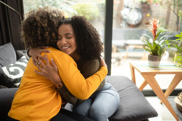 An African-American female psychotherapist comforts the teenage female patient by hugging her. Both of them have the afro hairstyle.
