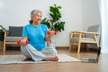 Asian senior woman lifting dumbbell for exercise and workout at home. Active mature woman doing...