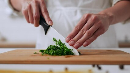 The process of cutting greens in the home kitchen, a cook in a white apron cuts greens with a ceramic knife for cooking food for vegans non-protein food for diet
