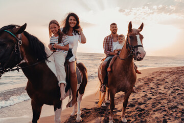 The family spends time with their children while riding horses together on a sandy beach. Selective focus  - obrazy, fototapety, plakaty