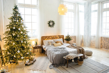 Cozy eco-style bedroom decorated for Christmas. Double bed with pillows and blankets near a large...