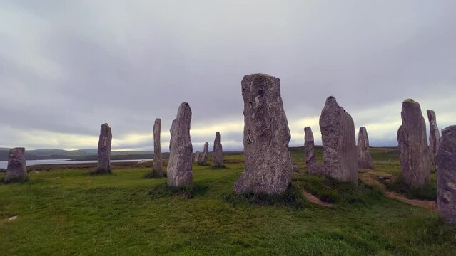 Moving around the standing stones or megaliths of the Callanish or Calanais stone circle in a cloudy evening. Sun peeking through the could, magic, ancient, neolithic atmosphere. Archaeological sites.