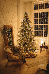 Warm Christmas evening in the interior of a room with a cozy wicker chair near a large Christmas tree, decorated with a lot of garland lights and white toys. New Year's Eve, festive Christmas interior