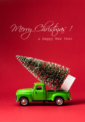 Green retro toy car carrying a Christmas tree on red background with text - Merry Christmas and Happy New Year. Christmas and New Year celebration concept. Greeting card. Copy space, selective focus