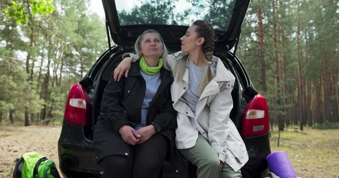 Concept of happy relationship between mother and daughter sitting in open trunk happy young daughter hugging elderly mother talking women in forest spending time together women resting after hard road