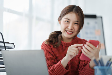 Pretty freelance asian business woman using mobile phone at working table in modern office.