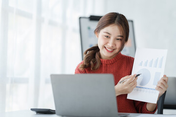 Confident Asian female office worker freelancer working in office, wearing red sweater, thai people.