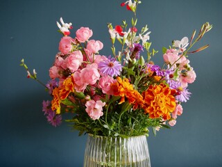 Close up of colorful garden flowers in glass vase against petrol blue wall.