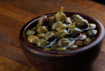 A bowl of pickled capers stands on a wooden surface.