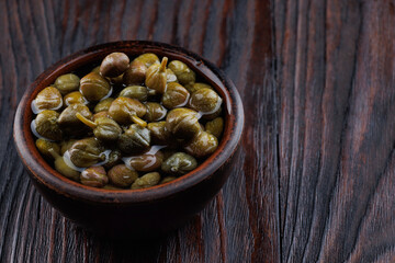 Pickled capers in a clay cup on a wooden table.