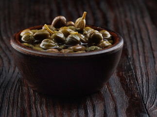 Pickled capers in a clay cup on a wooden table.