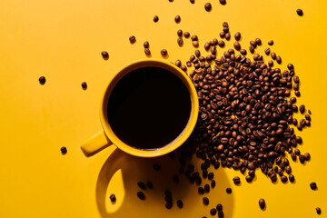 Cup of freshly brewed roasted coffee beans on yellow background