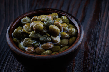 An earthenware bowl filled to the brim with capers stands on a wooden table.