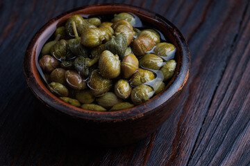 An earthenware bowl filled to the brim with capers stands on a wooden table.