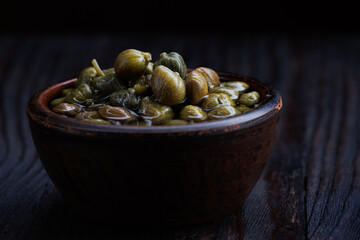 An earthenware bowl filled to the brim with capers stands on a wooden table.