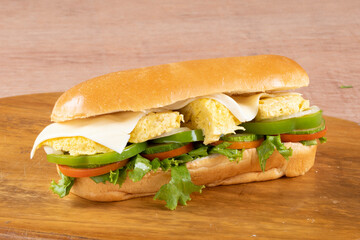 fresh submarine sandwiches with ham, cheese, bacon, tomatoes, lettuce, cucumbers and onions on dark wooden background