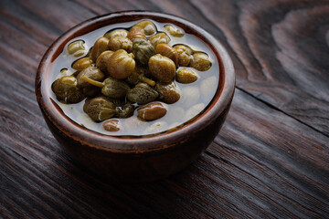 Capers in a clay cup standing on a wooden table.