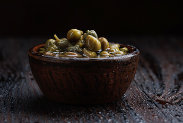 Pickled capers in brine. Clay cup full of capers.