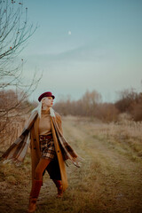 Fashionable elegant blonde woman wearing trendy autumn outfit with classic brown coat, trendy cap, plaid scarf, turtleneck, mini wrap skirt, leather boots, walking outdoor. Full-length portrait

