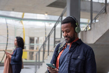African American businessman waiting for train on platform with smartphone in hand and headphones