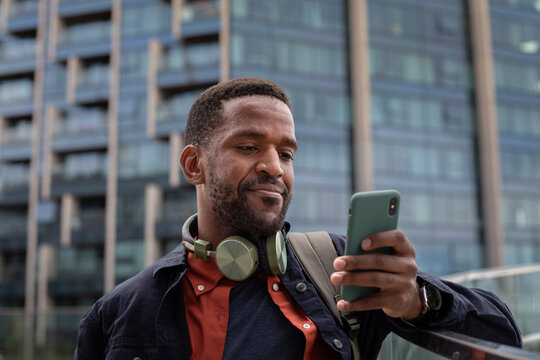 African American businessman using smartphone in city surrounded by office buildings
