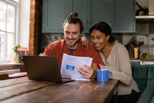 Happy young adult couple at home looking at personal finances using a laptop