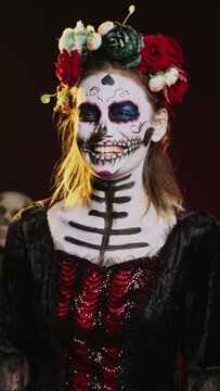 Vertical video: Holy mexican entity laughing and acting scary in studio, looking like la cavalera catrina on day of the dead traditional holiday. Smiling and wearing halloween costume with flowers