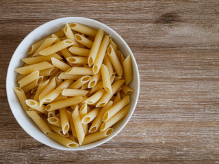 Penne-Pasta in einer weißen Porzelanschale auf einem Echtholztisch bei natürlichem Licht