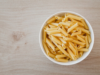 Penne-Pasta in einer weißen Porzelanschale auf einem Echtholztisch bei natürlichem Licht