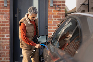 Mid adult male plugging in electric car to charge at home