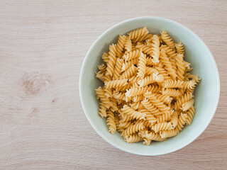 Spirelli / Fusilli / Spiral-Pasta in einer grünen Porzelanschale auf einem Echtholztisch bei natürlichem Licht