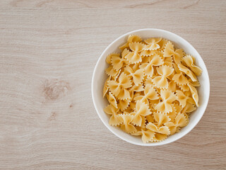 Farfalle-Pasta / Schmetterlingsnudeln  in einer weißen Porzelanschale auf einem Echtholztisch bei natürlichem Licht