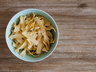 Bandnudel Pasta in einer grünen Porzelanschale auf einem Echtholztisch bei natürlichem Licht