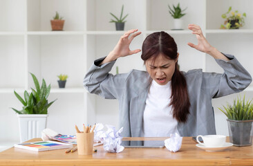 Mad Angry Stressed young asian female graphic designer or businesswoman with a crumpling paper on the table dissatisfied with her work, complained from her boss, getting a job problem.