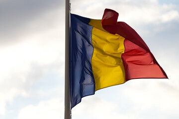 Flag of Romania winding against blue sky background with white clouds. Concept image to represent Romania.