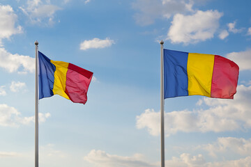 Two flags of Romania winding against blue sky with white clouds. Concept image that represent the country of Romania.