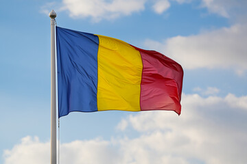 Flag of Romania winding against blue sky background with white clouds. Concept image to represent...