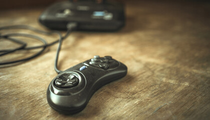 A black joystick from a 90's video game console is lying on a wooden table. A television game console of the last century. © Svetliy