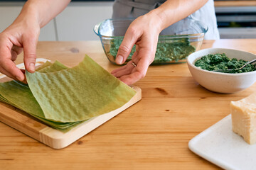 Hands of woman preparing homemade spinach and ricotta lasagna. Traditional Italian dish. Selective focus.