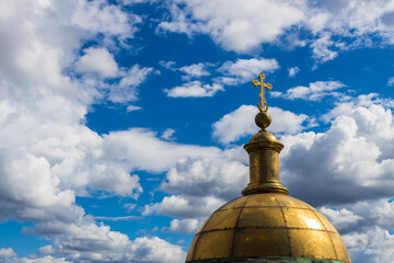 Gilded dome and cross of a religious temple against a blue sky with clouds. Religion and culture.