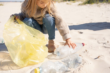  little girl with trash bag cleaning up the beach. Child collects plastic, garbage on the beach by...