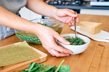 Hands of woman preparing homemade spinach and ricotta lasagna. Traditional Italian dish. Selective focus.