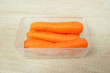 Fresh carrots in transparent container on table top view