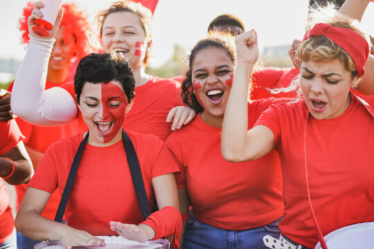 Group of multiracial young sport suppoters screaming outside of stadium - Fans wwearing red shirts having fun together outside with drums